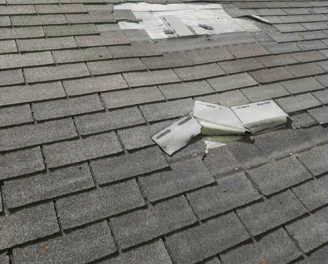 Residential roof showing wind damage and exposed underlayment after storm